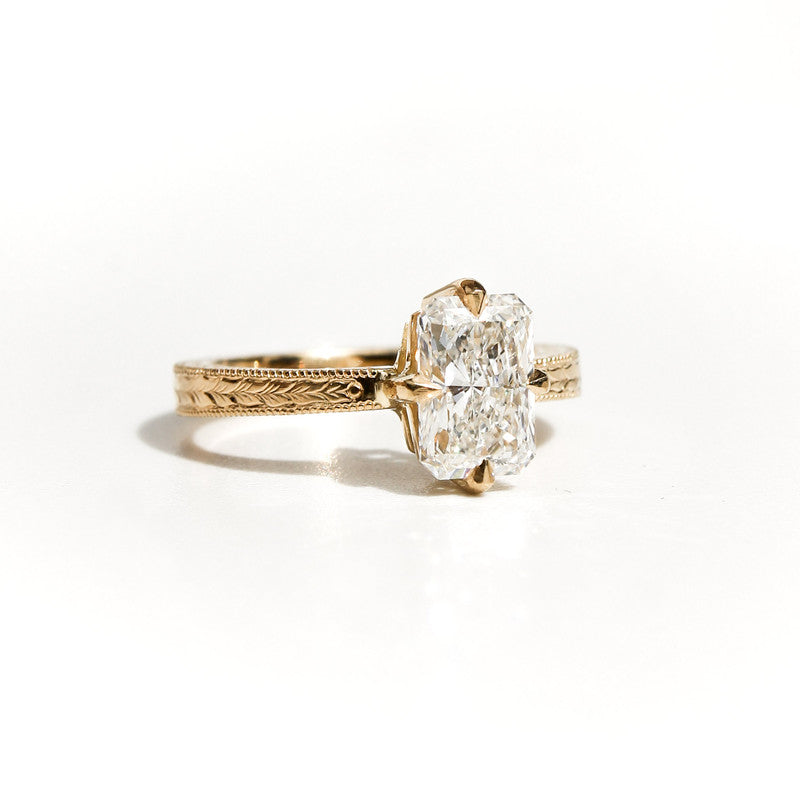 Anillo de oro amarillo con grabados artesanales y diamante rectangular brillante sobre fondo blanco.