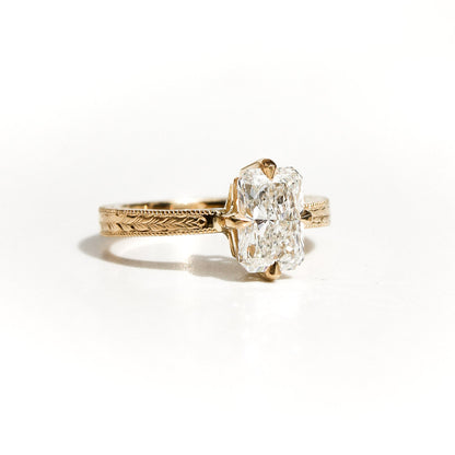 Anillo de oro amarillo con grabados artesanales y diamante rectangular brillante sobre fondo blanco.
